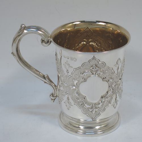 A very pretty Antique Victorian Sterling Silver christening mug, having a round body with straight tapering sides and tucked under belly, with hand-chased floral and scroll-work decoration surrounding four vacant lobed cartouches, a scroll loop handle, a gold-gilt interior, and all sitting on a pedestal foot. Made by Robert Hennell of London in 1865. The dimensions of this fine hand-made antique silver christening mug are height 10 cms (4 inches), diameter at lip 7 cms (2.75 inches), and it weighs approx. 130g (4.2 troy ounces).  