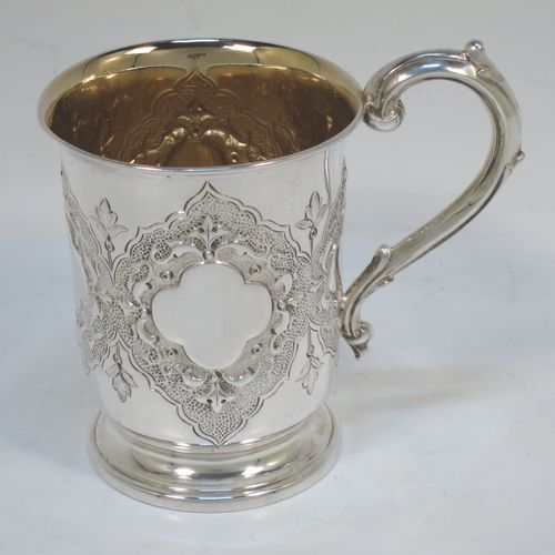 A very pretty Antique Victorian Sterling Silver christening mug, having a round body with straight tapering sides and tucked under belly, with hand-chased floral and scroll-work decoration surrounding four vacant lobed cartouches, a scroll loop handle, a gold-gilt interior, and all sitting on a pedestal foot. Made by Robert Hennell of London in 1865. The dimensions of this fine hand-made antique silver christening mug are height 10 cms (4 inches), diameter at lip 7 cms (2.75 inches), and it weighs approx. 130g (4.2 troy ounces).  