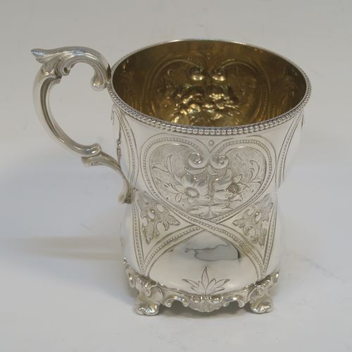 A very pretty Antique Victorian Sterling Silver christening mug, having a round bellied body with hand-chased floral and scroll-work decoration, an applied bead-edged top border, a cast scroll side-handle, a gold-gilt interior, and all sitting on four cast foliate feet. This beautiful antique silver christening mug was made by Elizabeth and John Eaton of London in 1862. The dimensions of this fine hand-made antique silver christening mug are height 10 cms (4 inches), diameter at lip 7.5 cms (3 inches), and it weighs approx. 130g (4.2 troy ounces).  