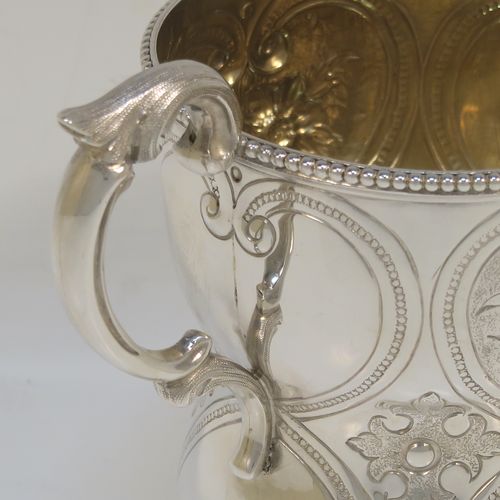 A very pretty Antique Victorian Sterling Silver christening mug, having a round bellied body with hand-chased floral and scroll-work decoration, an applied bead-edged top border, a cast scroll side-handle, a gold-gilt interior, and all sitting on four cast foliate feet. This beautiful antique silver christening mug was made by Elizabeth and John Eaton of London in 1862. The dimensions of this fine hand-made antique silver christening mug are height 10 cms (4 inches), diameter at lip 7.5 cms (3 inches), and it weighs approx. 130g (4.2 troy ounces).  