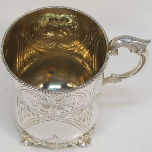 A very pretty Antique Victorian Sterling Silver christening mug, having a round bellied body with hand-chased floral and scroll-work decoration, an applied bead-edged top border, a cast scroll side-handle, a gold-gilt interior, and all sitting on four cast foliate feet. This beautiful antique silver christening mug was made by Elizabeth and John Eaton of London in 1862. The dimensions of this fine hand-made antique silver christening mug are height 10 cms (4 inches), diameter at lip 7.5 cms (3 inches), and it weighs approx. 130g (4.2 troy ounces).  