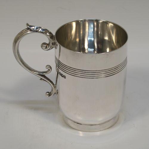 A very handsome Antique Sterling Silver christening mug, having a plain round body with a band of hand-chased reeded decoration and a tucked under belly, a cast scroll side-handle, and sitting on a round collet foot. This elegant silver christening mug was made by William Hutton and Sons of Sheffield in 1918. The dimensions of this fine hand-made antique silver christening mug are height 9 cms (3.5 inches), length 10 cms (4 inches), and it weighs approx. 147g (4.7 troy ounces).   