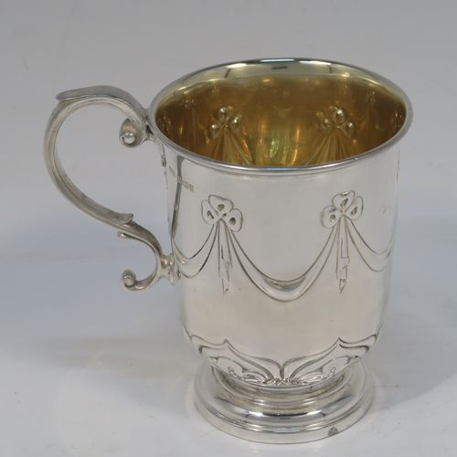 A very pretty Antique Edwardian Sterling Silver christening mug, having a round bellied body, with hand-chased ribbons, swags, and lotus leaf decoration, a cast scroll side-handle, a gold-gilt interior, and sitting on a pedestal foot. This beautiful antique silver christening mug was made by James Dixon and Sons of Sheffield in 1910. The dimensions of this fine hand-made antique silver christening mug are height 10 cms (4 inches), length 10 cms (4 inches), and it weighs approx. 151g (4.9 troy ounces).   