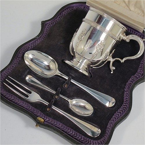 A Sterling Silver christening set consisting of a christening mug with applied strap-work decoration and a scroll handle, and a matching fork and two spoons in the Rattail Hanoverian pattern, all in a cream satin and blue velvet-lined presentation box. The christening mug made in London 1919 and the cutlery from 1895 to 1928. The dimensions of this fine hand-made antique silver christening set are height of mug 9 cms (3.7 inches), length of fork 16 cms (6.25 inches), and with a total weight of approx. 280g (9 troy ounces).   