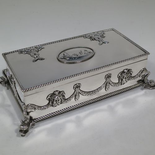 A very handsome and unusual Neptune themed Antique Victorian Sterling Silver cigar / cigarette box, having a rectangular body with applied rope-twist borders, laurel-leaf swags, Neptune face masks, and inter-twined dolphins, a hinged lid with an applied central oval cartouche with a scene of Neptune, mermaids, and sea-horses, a varnished wood-lined interior, and all sitting on four cast dolphin feet. Made by Reid and Sons of London in 1901. The dimensions of this fine hand-made antique silver table box are length 26 cms (10 inches), width 14 cms (5.5 inches), and height 8 cms (3 inches).    