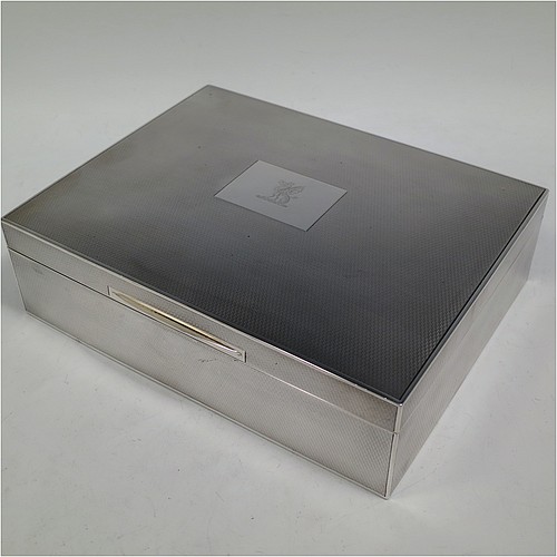 A large and handsome Sterling Silver cigarette or cigar humidor table box, having a rectangular straight-sided body with all over engine-turned decoration, a hinged lid having an applied thumb-piece and central cartouche, a gold-gilt and cedar wood-lined interior, with two removable dividers. Made by Goldsmiths and Silversmiths of London in 1937. The dimensions of this fine hand-made silver table box are length 23 cms (9 inches), width 18 cms (7 inches), and height 7 cms (2.75 inches). Please note that this item is crested on the cartouche.   