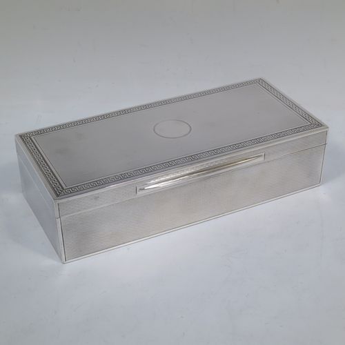 A very elegant Antique Sterling Silver cigarette / cigar table box, having a rectangular body with geometrically designed engine-turned decoration, a hinged lid with a central round vacant cartouche and a Greek-Key border, an applied thumb-piece, a gold-gilt and cedar wood-lined interior, and all sitting on a flat base. Made by Mappin and Webb of London in 1919. The dimensions of this fine hand-made antique silver table box are length 20 cms (8 inches), width 9 cms (3.5 inches), and height 5 cms (2 inches).   