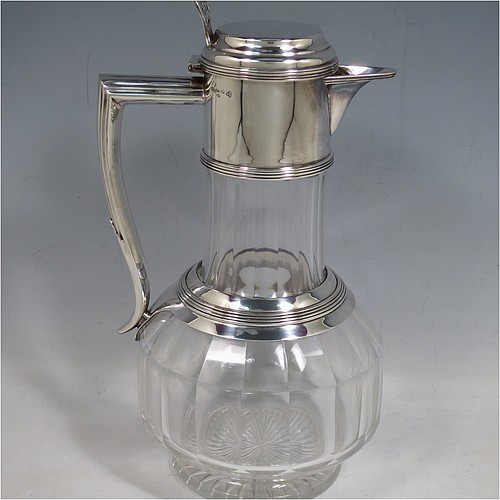 An Antique Victorian Silver Plated and hand-cut crystal claret jug, having a plain round mount with applied reeded borders, a stepped lid with a hand-pierced thumb-piece, a flat-topped scroll handle attached to a round and reeded security ring, together with a hand-cut round, panelled, and bellied crystal body with star-cut base. Made by William Hutton and Sons of Sheffield in 1880. The dimensions of this fine hand-made antique silver plated and crystal claret jug are height 24 cms (9.5 inches), and length 15 cms (6 inches).    