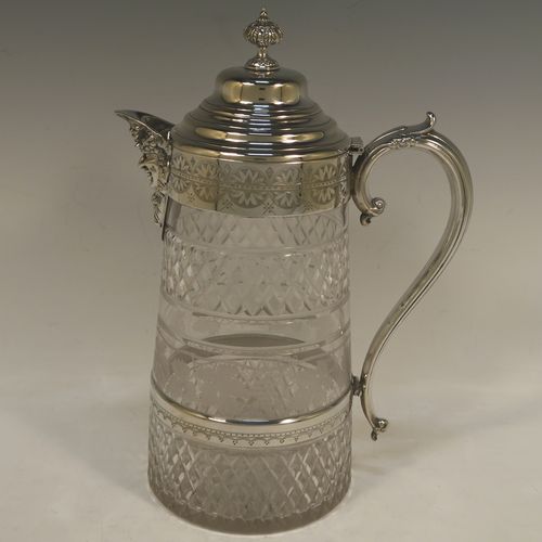 A very handsome and large Antique Victorian Silver Plated and hand-cut crystal claret jug, having a hand-engraved mount with floral decoration, a Bacchus face on the spout, a hinged stepped and domed lid with cast finial, a scroll side handle attached to a lower strengthening girdle, and a round hand-cut straight-sided body with a single band of hand-engraved frosted cut work in a grapevine pattern with two bands of hobnail pattern above and below, all sitting on a flat base with a star-cut. Made in ca.1880. The dimensions of this fine hand-made antique silver-plated and crystal claret jug are height 29 cms (11.5 inches), length 20 cms (8 inches), and diameter at the base is 13 cms (5 inches). 