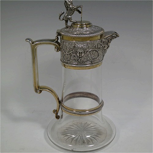 A very handsome Antique Victorian Silver Plated and hand-cut crystal claret jug, having an ornate parcel gilt Bacchus style round mount with hand-chased grapevine work, a sided handle with a bead-edged security ring, a hinged lid with a cast rampant lion and shield finial, together with a hand-cut crystal round body with straight sides and a tucked under belly above a flat star-cut base. Made by Elkington and Co., of Sheffield, with a date letter for 1883. The dimensions of this fine hand-made antique silver-plated and crystal claret jug are height 27 cms (10.5 inches), and length 16 cms (6.25 inches). Please note that this item is monogrammed on the finial shield.    