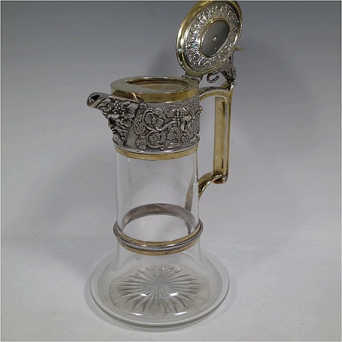 A very handsome Antique Victorian Silver Plated and hand-cut crystal claret jug, having an ornate parcel gilt Bacchus style round mount with hand-chased grapevine work, a sided handle with a bead-edged security ring, a hinged lid with a cast rampant lion and shield finial, together with a hand-cut crystal round body with straight sides and a tucked under belly above a flat star-cut base. Made by Elkington and Co., of Sheffield, with a date letter for 1883. The dimensions of this fine hand-made antique silver-plated and crystal claret jug are height 27 cms (10.5 inches), and length 16 cms (6.25 inches). Please note that this item is monogrammed on the finial shield.    