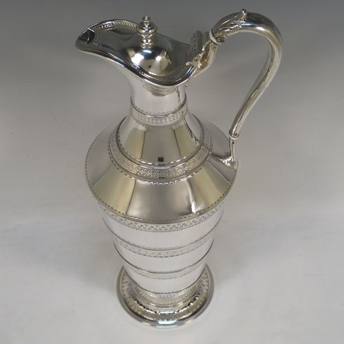 A very unusual Antique Victorian Silver Plated  claret or water jug ewer, having a round body with tapering sides and bands of hand-engraved floral and geometric decoration, an insulated side handle, a hinged lid with an urn finial, and all sitting on a pedestal foot. This beautiful antique silver-plated ewer was made in ca. 1880. The dimensions of this fine hand-made antique silver-plated claret jug are height 32 cms (12.5 inches), and length 15 cms (6 inches).   