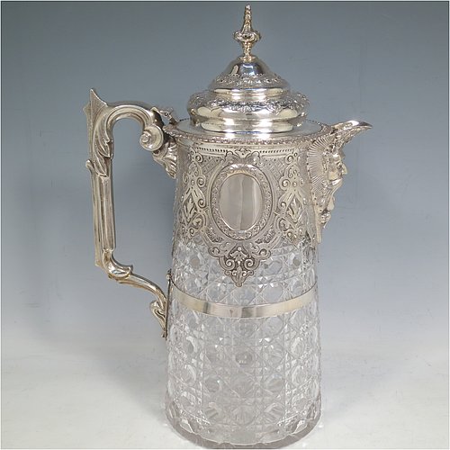 An Antique Victorian Sterling Silver and hand-cut crystal claret jug, having a hand-chased mount with floral decoration, oval vacant cartouches either side, a Bacchus face spout, a hinged lid with floral chasing and a cast finial, a cast scroll handle attached to a retaining ring, together with a hand-cut crystal body with hobnail-cut pattern. Made by Charles Boyton of London in 1882. The dimensions of this fine hand-made antique silver and crystal claret jug are height 29 cms (11.5 inches), and length 19 cms (7.5 inches).   