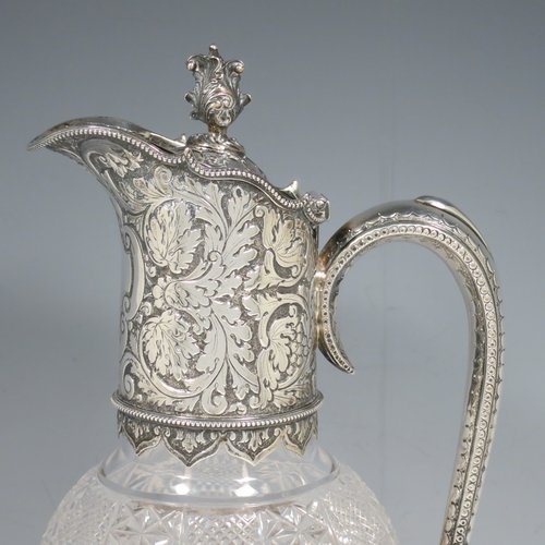 An Antique Victorian Sterling Silver and hand-cut crystal claret jug, having a hand-chased mount with floral decoration and a wavey bead-edged border, a hinged lid with cast floral finial, a hand-chased and engraved scroll handle attached to a hand-pierced floral band, together with an oval cross-section hand-cut Webb crystal body with star-cut panels, all sitting on a matching collet foot. Made by Gibson & Langland of London in 1890. The dimensions of this fine hand-made antique silver and crystal claret jug are height 31 cms (12.25 inches), and length 15 cms (6 inches).   