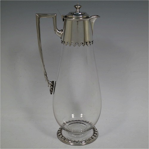 A very handsome Antique Victorian Silver Plated and hand-cut crystal claret jug, having a plain round mount with a bead-work border and hand-cut fleur-de-lis decoration, a hinged stepped lid with cast finial, a plain angular handle and a sparrow-beak style spout, together with a hand-cut crystal body with tapering sides and tucked under belly, and sitting on a collet foot with a matching bead and hand-cut cover. Made by William Hutton and Sons of Sheffield in ca. 1890. The dimensions of this fine hand-made antique silver-plated and crystal claret jug are height 28.5 cms (11.25 inches), and length 12.5 cms (5 inches).    