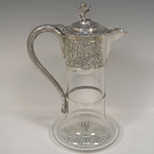 A very handsome Antique Victorian Sterling Silver and hand-cut crystal claret jug, having an ornate Bacchus style round mount with hand-chased grapevine work, a tendril style sided handle with a security ring, a hinged lid with a cast rampant lion and shield finial, together with a hand-cut crystal round body with straight sides and a tucked under belly above a flat star-cut base. This beautiful antique silver claret jug was made by Charles Boyton of London in 1889. The dimensions of this fine hand-made antique silver and crystal claret jug are height 27 cms (10.5 inches), and length 18.5 cms (7.5 inches).   