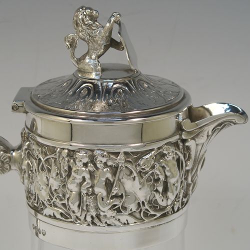 A very handsome Antique Victorian Silver Plated and hand-cut crystal claret jug, having an ornate  Bacchus style round mount with hand-chased figural work, a cast side handle with a plain round security ring, a hinged lid with a cast rampant lion and shield finial, together with a hand-cut crystal round body with straight sides and a tucked under belly above a flat star-cut base. Made by Hukin and Heath  of Sheffield in ca. 1880. The dimensions of this fine hand-made antique silver-plated and crystal claret jug are height 26 cms (10.25 inches), and length 16 cms (6.3 inches).  