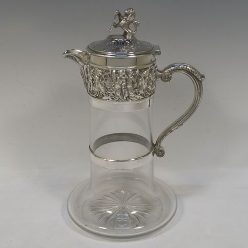 A very handsome Antique Victorian Silver Plated and hand-cut crystal claret jug, having an ornate  Bacchus style round mount with hand-chased figural work, a cast side handle with a plain round security ring, a hinged lid with a cast rampant lion and shield finial, together with a hand-cut crystal round body with straight sides and a tucked under belly above a flat star-cut base. Made by Hukin and Heath  of Sheffield in ca. 1880. The dimensions of this fine hand-made antique silver-plated and crystal claret jug are height 26 cms (10.25 inches), and length 16 cms (6.3 inches).  