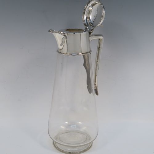 A very elegant Antique Victorian Silver Plated and hand-cut crystal claret jug, having a plain round mount with applied bead-edged borders, a plain side handle with a vertical strengthening strut, a hinged domed lid with a plain thumb-piece, together with a hand-cut crystal round body with straight tapering sides and a tucked under belly above a pedestal foot. This handsome silver-plated and crystal claret jug was made in ca. 1890. The dimensions of this fine hand-made antique silver-plated and crystal claret jug are height 28 cms (11 inches), and length 12.5 cms (5 inches). Please note that this item is crested.   