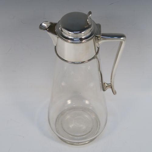 A very elegant Antique Victorian Silver Plated and hand-cut crystal claret jug, having a plain round mount with applied bead-edged borders, a plain side handle with a vertical strengthening strut, a hinged domed lid with a plain thumb-piece, together with a hand-cut crystal round body with straight tapering sides and a tucked under belly above a pedestal foot. This handsome silver-plated and crystal claret jug was made in ca. 1890. The dimensions of this fine hand-made antique silver-plated and crystal claret jug are height 28 cms (11 inches), and length 12.5 cms (5 inches). Please note that this item is crested.   