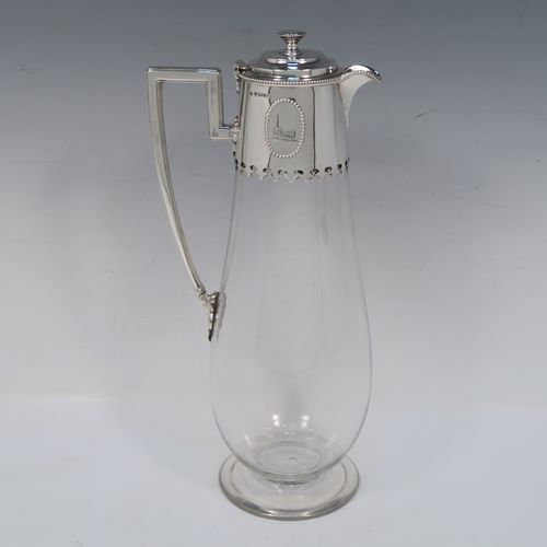 A very elegant Antique Victorian Sterling Silver and hand-cut crystal claret jug, having a plain round mount with applied bead-edged borders, a plain square cross-section side handle, a hinged stepped lid with a cast round finial, together with a hand-cut crystal round body with straight tapering sides and a tucked under belly above a pedestal foot. This handsome silver and crystal claret jug was made by Charles Favell of Sheffield in 1875. The dimensions of this fine hand-made antique silver and crystal claret jug are height 28 cms (11 inches), and length 13.5 cms (5.25 inches). Please note that this item has two oval cartouches with bead borders one of which is  engraved with a part crest.   