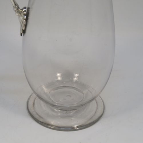 A very elegant Antique Victorian Sterling Silver and hand-cut crystal claret jug, having a plain round mount with applied bead-edged borders, a plain square cross-section side handle, a hinged stepped lid with a cast round finial, together with a hand-cut crystal round body with straight tapering sides and a tucked under belly above a pedestal foot. This handsome silver and crystal claret jug was made by Charles Favell of Sheffield in 1875. The dimensions of this fine hand-made antique silver and crystal claret jug are height 28 cms (11 inches), and length 13.5 cms (5.25 inches). Please note that this item has two oval cartouches with bead borders one of which is  engraved with a part crest.   