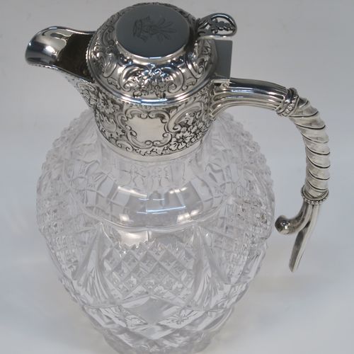 A very beautiful Antique Victorian Sterling Silver and hand-cut crystal claret jug, having an ornate round mount with hand-chased floral and scroll decoration, a fluted and twisted style side handle, a hinged lid with matching decoration and a pierced thumb-piece, together with a hand-cut crystal round body with tapering sides and above a flat star-cut base. This beautiful antique silver and crystal claret jug was made by Gibson and Langland of London in 1898. The dimensions of this fine hand-made antique silver and crystal claret jug are height 23 cms (9 inches), and length 14 cms (5.5 inches). Please note that this item is crested on the top of the lid.