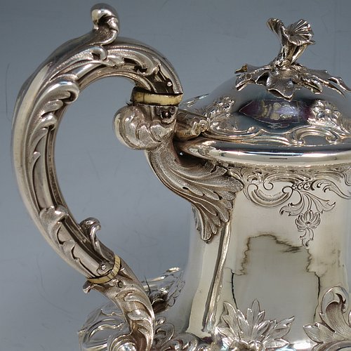 An Antique Georgian William IV Sterling Silver hand-chased coffee pot, having a round hand-chased bellied body with floral and scroll decoration, a hinged lid with original cast flower finial, an insulated silver handle with anthemion thumb-piece, and sitting on cast floral and scroll feet. Made by the Barnard Brothers of London in 1832. The dimensions of this fine hand-made antique silver coffee pot are height 25 cms (9.75 inches), length 25.5 cms (10 inches), and it weighs approx. 978g (31.5 troy ounces).   