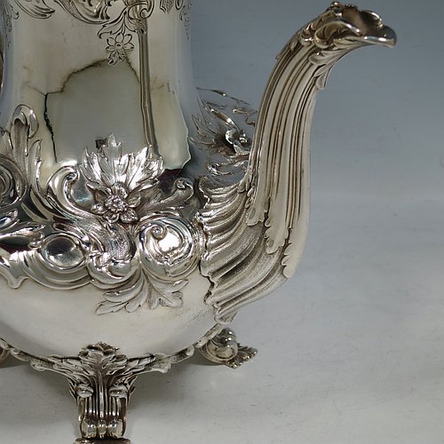 An Antique Georgian William IV Sterling Silver hand-chased coffee pot, having a round hand-chased bellied body with floral and scroll decoration, a hinged lid with original cast flower finial, an insulated silver handle with anthemion thumb-piece, and sitting on cast floral and scroll feet. Made by the Barnard Brothers of London in 1832. The dimensions of this fine hand-made antique silver coffee pot are height 25 cms (9.75 inches), length 25.5 cms (10 inches), and it weighs approx. 978g (31.5 troy ounces).   