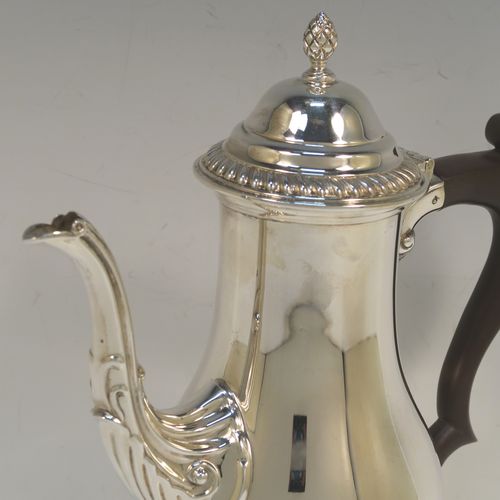 A very handsome Sterling Silver coffee pot in a Georgian style, having a plain round bellied body with applied gadroon borders, a brown wooden scroll handle, a hinged domed lid with a cast pineapple finial, and sitting on a pedestal feet. This beautiful silver coffee pot was made by the Barker Brothers of Birmingham in 1969. The dimensions of this fine hand-made silver coffee pot are height 23 cms (9 inches), length 18.5 cms (7.25 inches), and it weighs approx. 450g (14.5 troy ounces).  