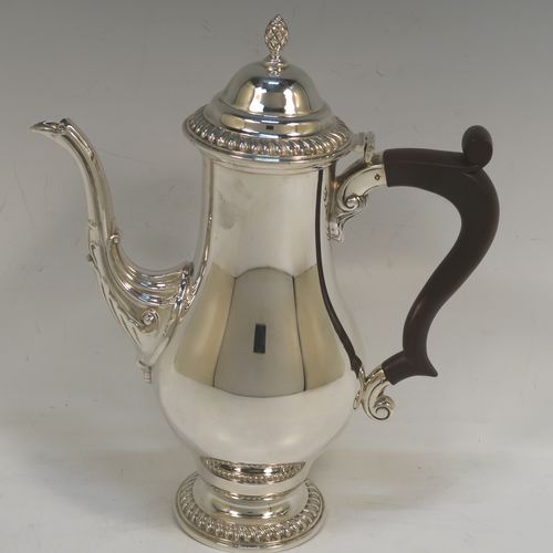 A very handsome Sterling Silver coffee pot in a Georgian style, having a plain round bellied body with applied gadroon borders, a brown wooden scroll handle, a hinged domed lid with a cast pineapple finial, and sitting on a pedestal feet. This beautiful silver coffee pot was made by the Barker Brothers of Birmingham in 1969. The dimensions of this fine hand-made silver coffee pot are height 23 cms (9 inches), length 18.5 cms (7.25 inches), and it weighs approx. 450g (14.5 troy ounces).  