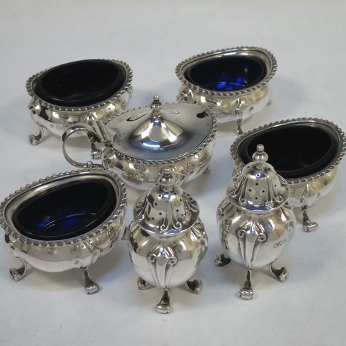 A handsome and large Antique Edwardian Sterling Silver seven-piece condiment service, consisting of a mustard pot with hinged lid and blue-glass liner, four salt cellars with blue-glass liners, and two pepper pots with pull-off lids, all with scroll fluted bellied bodies and sitting four scroll feet, and all fitted into their original dark blue satin and velvet-lined red presentation box. Made by James Round of London  in 1903. The dimensions of this fine hand-made condiment service are height of pepper pot 9 cms (3.5 inches), length of mustard pot 9 cms (3.5 inches), and with a total weight of approx. 353g (11.4 troy ounces).   