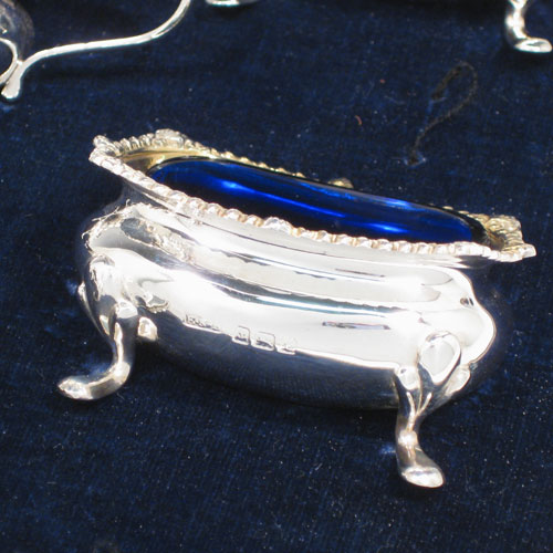 Sterling silver eight-piece condiment set, consisting of four open salt cellars with blue-glass liners, two mustard pots with hinged lids, and two pepper shakers, all with plain baluster bodies, gadroon borders, and sitting on four foliate feet, and all fitted into an original satin and velvet-lined presentation box. Made by E. S. Barnsley & Co., of Birmingham in 1918. The dimensions of this fine hand-made silver condiment service are height of pepper pots 8 cms (3 inches), length of mustard pots 8 cms (3 inches), and with a total weight of approx. 255g (8.2 troy ounces).