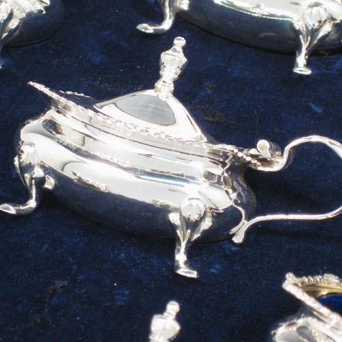 Sterling silver eight-piece condiment set, consisting of four open salt cellars with blue-glass liners, two mustard pots with hinged lids, and two pepper shakers, all with plain baluster bodies, gadroon borders, and sitting on four foliate feet, and all fitted into an original satin and velvet-lined presentation box. Made by E. S. Barnsley & Co., of Birmingham in 1918. The dimensions of this fine hand-made silver condiment service are height of pepper pots 8 cms (3 inches), length of mustard pots 8 cms (3 inches), and with a total weight of approx. 255g (8.2 troy ounces).