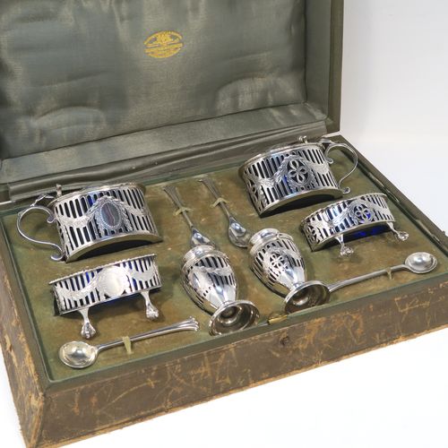 A large and heavy Antique Sterling Silver six-piece condiment service in a Neoclassical style with hand-pierced and laurel-leaf swags decoration, all with interior blue glass liners, and claw and ball feet. Consisting of two mustard pots with domed hinged lids, two salt cellars, two pepper pots with bayonet fit lids, and together with their original condiment spoons in the Onslow pattern, and all fitted into their original light green satin and velvet-lined presentation box. This beautiful condiment service was made by Goldsmiths and Silversmiths of London in 1925 to 1929. The dimensions of this fine hand-made antique silver condiment service are height of pepper pots 6.5 cms (2.5 inches), length of mustard pots 9 cms (3.5 inches), and with a total weight of approx. 327g (10.5 troy ounces).   