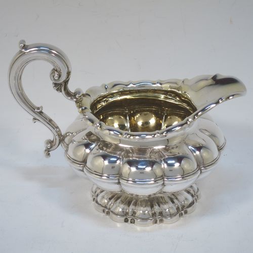 A very pretty Antique late Georgian Sterling Silver large cream jug, having a lobed round  body with hand-chased melon fluting, a scroll top border, a scroll handle with thumb-piece, a gold-gilt interior, and all sitting on a matching pedestal foot. Made by the Barnard Brothers of London in 1829. The dimensions of this fine hand-made antique silver cream jug are height 12 cms (4.75 inches), length 16 cms (6.25 inches), and it weighs approx. 233g (7.5 troy ounces).  