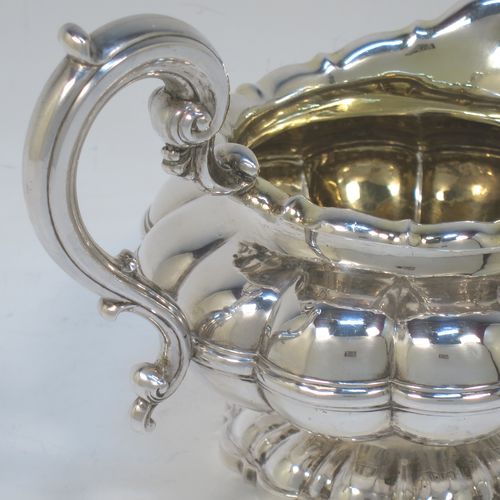 A very pretty Antique late Georgian Sterling Silver large cream jug, having a lobed round  body with hand-chased melon fluting, a scroll top border, a scroll handle with thumb-piece, a gold-gilt interior, and all sitting on a matching pedestal foot. Made by the Barnard Brothers of London in 1829. The dimensions of this fine hand-made antique silver cream jug are height 12 cms (4.75 inches), length 16 cms (6.25 inches), and it weighs approx. 233g (7.5 troy ounces).  