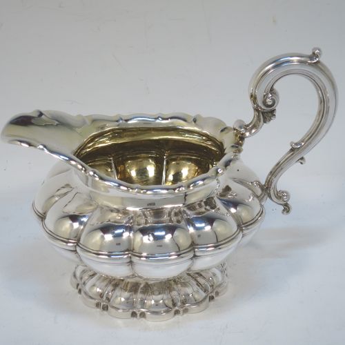 A very pretty Antique late Georgian Sterling Silver large cream jug, having a lobed round  body with hand-chased melon fluting, a scroll top border, a scroll handle with thumb-piece, a gold-gilt interior, and all sitting on a matching pedestal foot. Made by the Barnard Brothers of London in 1829. The dimensions of this fine hand-made antique silver cream jug are height 12 cms (4.75 inches), length 16 cms (6.25 inches), and it weighs approx. 233g (7.5 troy ounces).  