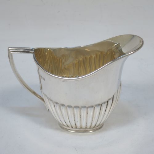 A pretty Antique Sterling Silver cream jug in a Queen Anne style, having an oval body with hand-chased half-fluted decoration, a reeded handle and applied reeded border, and all sitting on a collet foot. Made by Goldsmiths and Silversmiths of Sheffield in 1916. The dimensions of this fine hand-made antique silver cream jug are height 7.5 cms (3 inches), length 10 cms (4 inches), and it weighs approx. 55g (1.8 troy ounces).   