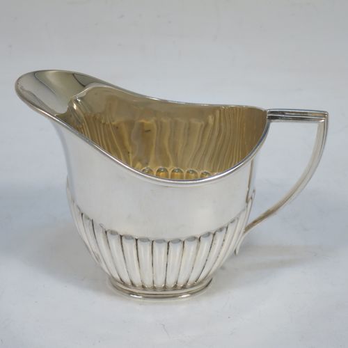 A pretty Antique Sterling Silver cream jug in a Queen Anne style, having an oval body with hand-chased half-fluted decoration, a reeded handle and applied reeded border, and all sitting on a collet foot. Made by Goldsmiths and Silversmiths of Sheffield in 1916. The dimensions of this fine hand-made antique silver cream jug are height 7.5 cms (3 inches), length 10 cms (4 inches), and it weighs approx. 55g (1.8 troy ounces).   