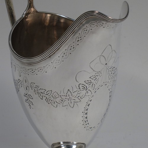 A very pretty Irish Antique Georgian Sterling Silver cream jug, having a round body with tapering sides in a Helmet style, with hand-engraved swags of floral decoration, a vacant oval cartouche, an applied reeded border, a scroll handle, and sitting on a pedestal foot with a round base. Made by Matthew West of Dublin in 1789. The dimensions of this fine hand-made antique Irish silver cream jug are length 11.5 cms (4.5 inches), height 16 cms (6.25 inches), and it weighs approx. 178g (5.7 troy ounces).