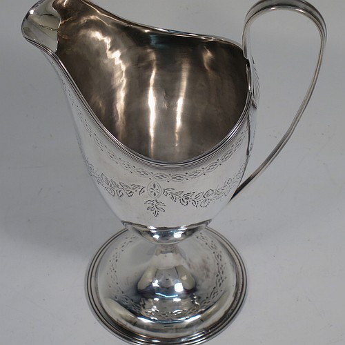 A very pretty Irish Antique Georgian Sterling Silver cream jug, having a round body with tapering sides in a Helmet style, with hand-engraved swags of floral decoration, a vacant oval cartouche, an applied reeded border, a scroll handle, and sitting on a pedestal foot with a round base. Made by Matthew West of Dublin in 1789. The dimensions of this fine hand-made antique Irish silver cream jug are length 11.5 cms (4.5 inches), height 16 cms (6.25 inches), and it weighs approx. 178g (5.7 troy ounces).