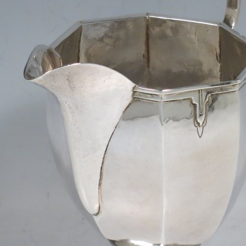 A Sterling Silver Arts & Crafts style large milk jug, having a panelled tapering body with a hand-hammered finish, an applied geometrical border, a plain handle and spout, and all sitting on a pedestal foot. Made by the Guild of Handicrafts of London in 1934. The dimensions of this fine hand-made silver cream or milk jug are height 13.5 cms (5.25 inches), length 15 cms (6 inches), and it weighs approx. 260g (8.4 troy ounces).    