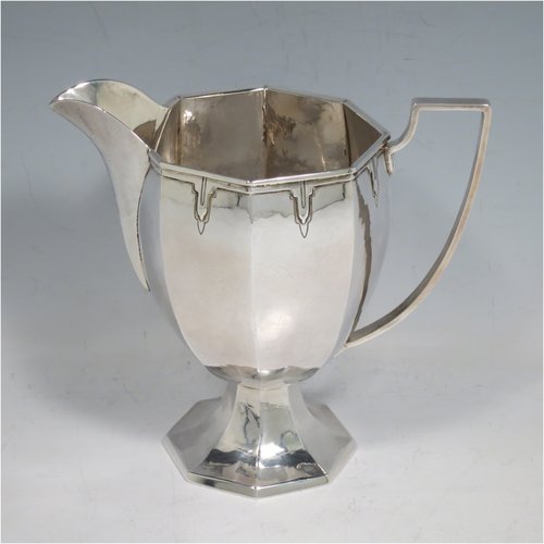 A Sterling Silver Arts & Crafts style large milk jug, having a panelled tapering body with a hand-hammered finish, an applied geometrical border, a plain handle and spout, and all sitting on a pedestal foot. Made by the Guild of Handicrafts of London in 1934. The dimensions of this fine hand-made silver cream or milk jug are height 13.5 cms (5.25 inches), length 15 cms (6 inches), and it weighs approx. 260g (8.4 troy ounces).    