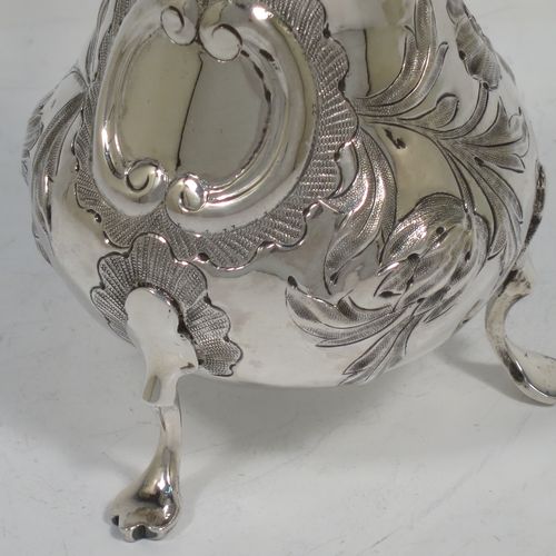 A very pretty Antique early Victorian Sterling Silver cream or milk jug having a round bellied body with hand-chased floral decoration surrounding a vacant cartouche, a scroll handle with anthemion leaf thumb-piece, a shaped border with a spout, a gold-gilt interior, and sitting on three cast trefoil feet. Made by William Hunter of London in 1845. The dimensions of this fine hand-made antique silver cream jug are height 11.5 cms (4.5 inches), length 10 cms (4 inches), and it weighs approx. 115g (3.7 troy ounces).    