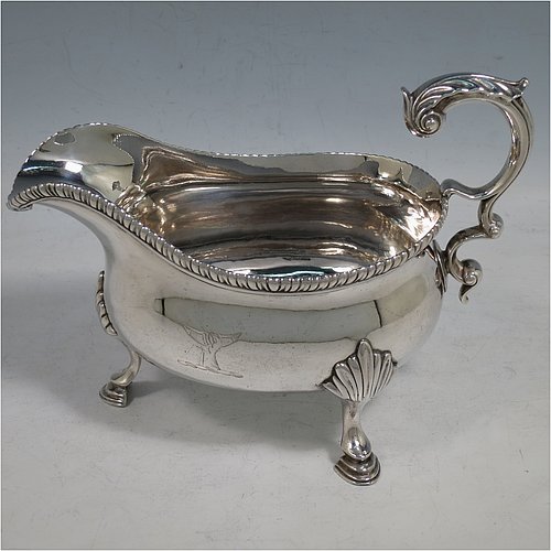 An Antique Georgian Sterling Silver pair of large and heavy George III sauce or gravy boats, having plain bellied bodies, with applied gadroon borders, cast scroll handles with anthemion leaf thumb-pieces, and sitting on three cast hoof feet with shell shoulders. Made by Thomas Wallis I of London in 1773. The dimensions of these fine hand-made antique silver gravy or sauce boats are length 18.5 cms (7.25 inches), width 10 cms (4 inches), height 14 cms (5.5 inches), and they weigh a total of 821g (26.5 troy ounces). Please note that these items are crested.