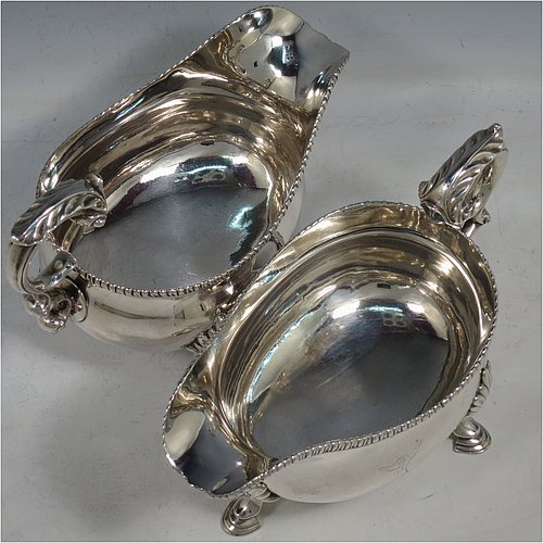 An Antique Georgian Sterling Silver pair of large and heavy George III sauce or gravy boats, having plain bellied bodies, with applied gadroon borders, cast scroll handles with anthemion leaf thumb-pieces, and sitting on three cast hoof feet with shell shoulders. Made by Thomas Wallis I of London in 1773. The dimensions of these fine hand-made antique silver gravy or sauce boats are length 18.5 cms (7.25 inches), width 10 cms (4 inches), height 14 cms (5.5 inches), and they weigh a total of 821g (26.5 troy ounces). Please note that these items are crested.