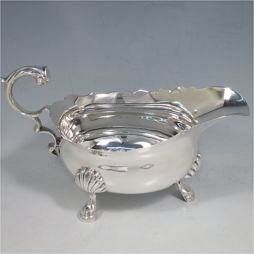 A Sterling Silver George II style large sauce or gravy boat, having a plain baluster, with a Chippendale border, a cast flying scroll handle, and sitting on three cast hoof feet with shell shoulders. Made by Edward Barnard of London in 1930. The dimensions of this fine hand-made silver sauce boat are length 20 cms (8 inches), width 9.5 cms (3.75 inches), height 11.5 cms (4.5 inches), and it weighs approx. 340g (11 troy ounces).    