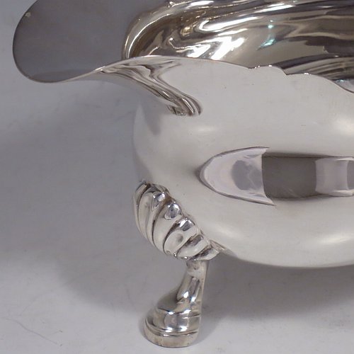 A Sterling Silver George II style large sauce or gravy boat, having a plain baluster, with a Chippendale border, a cast flying scroll handle, and sitting on three cast hoof feet with shell shoulders. Made by Edward Barnard of London in 1930. The dimensions of this fine hand-made silver sauce boat are length 20 cms (8 inches), width 9.5 cms (3.75 inches), height 11.5 cms (4.5 inches), and it weighs approx. 340g (11 troy ounces).    