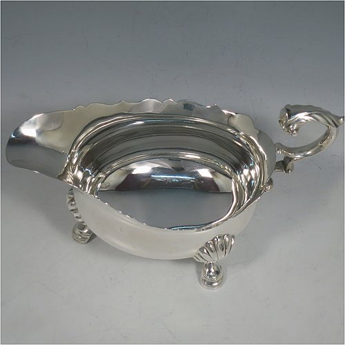 A Sterling Silver George II style large sauce or gravy boat, having a plain baluster, with a Chippendale border, a cast flying scroll handle, and sitting on three cast hoof feet with shell shoulders. Made by Edward Barnard of London in 1930. The dimensions of this fine hand-made silver sauce boat are length 20 cms (8 inches), width 9.5 cms (3.75 inches), height 11.5 cms (4.5 inches), and it weighs approx. 340g (11 troy ounces).    